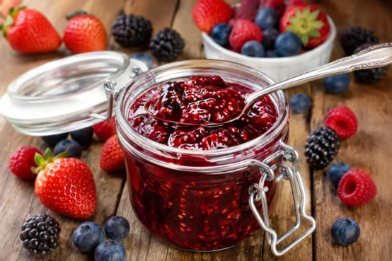 Geleia de frutas vermelhas caseira em pote de vidro com morangos, amoras, framboesas e mirtilos frescos